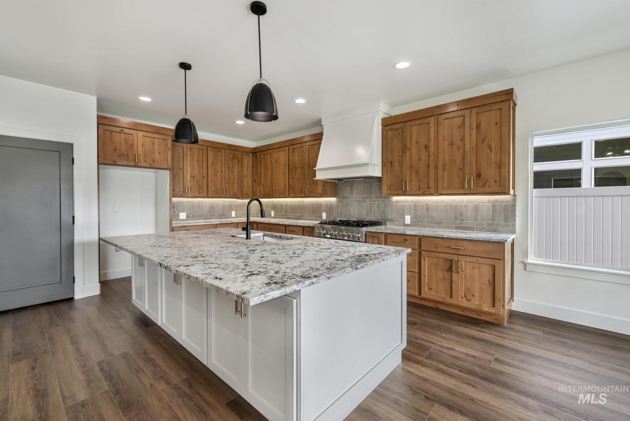 527 Falling Leaf Lane Twin Falls, ID 83301 - Photo 13 of 42 Kitchen with brown cabinetry, decorative light fixtures, premium range hood, light stone countertops, and tasteful backsplash