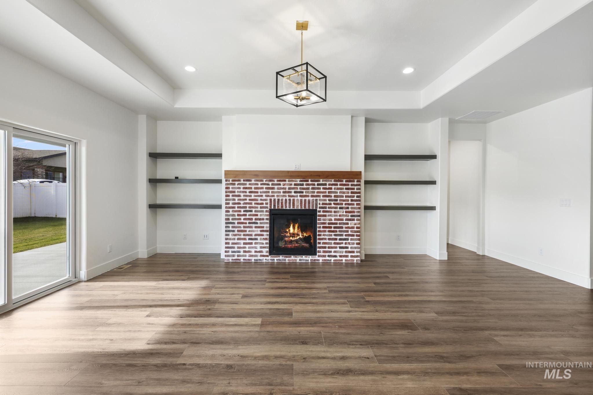 527 Falling Leaf Lane Twin Falls, ID 83301 - Photo 8 of 42 Unfurnished living room featuring built in features, dark wood-style flooring, a fireplace, a raised ceiling, and recessed lighting