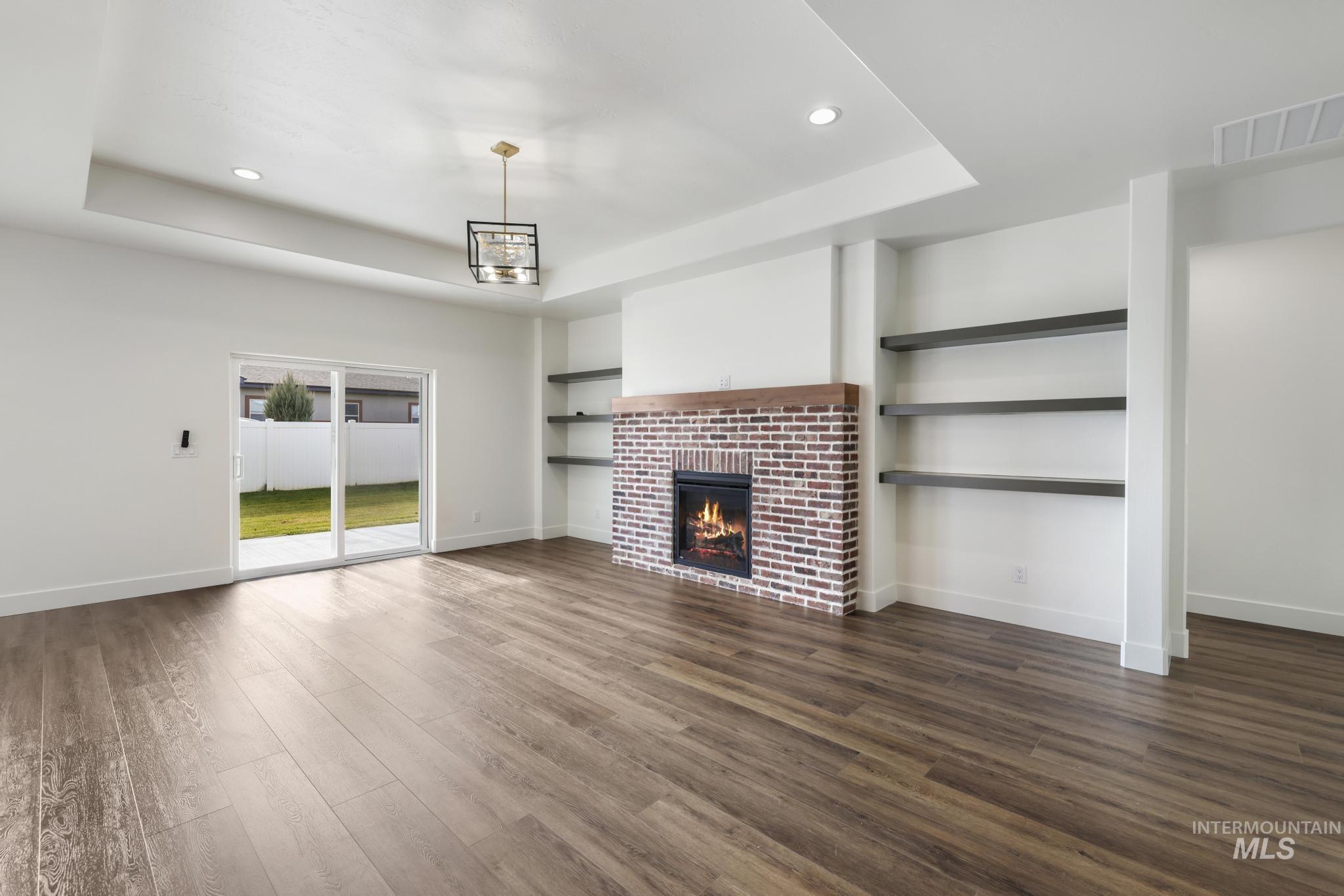 527 Falling Leaf Lane Twin Falls, ID 83301 - Photo 9 of 42 Unfurnished living room with a tray ceiling, recessed lighting, a tiled fireplace, dark wood-style flooring, and built in shelves