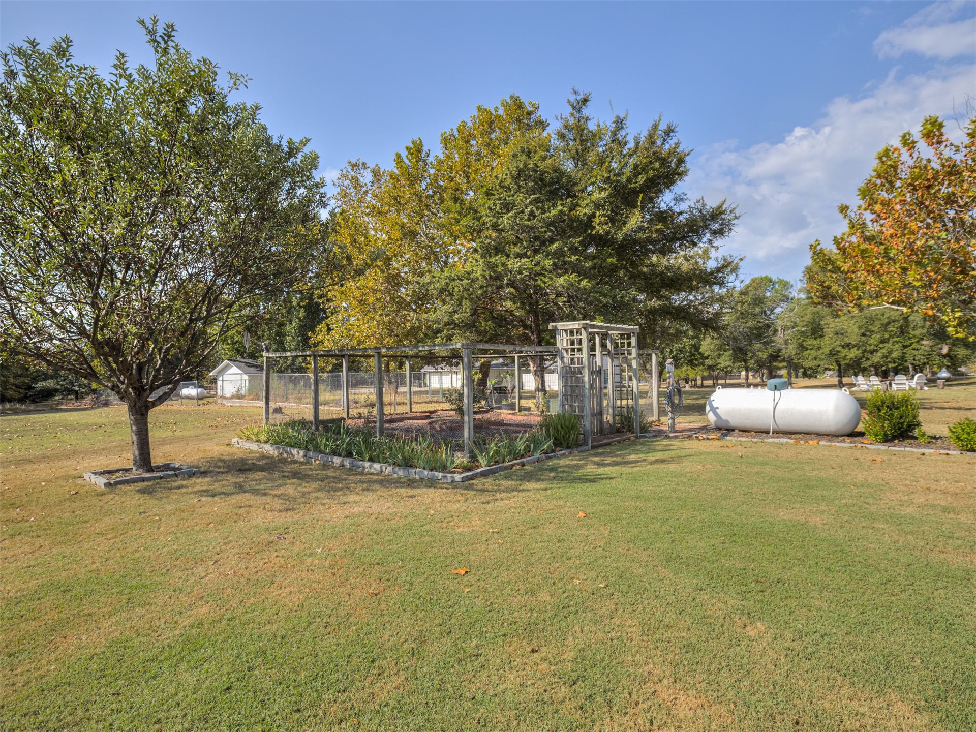 119 Mainsail Road Stigler, OK 74462 - Photo 44 of 52 Expansive lawn area featuring a large, established tree, a dedicated garden space with a trellis, and a visible propane tank