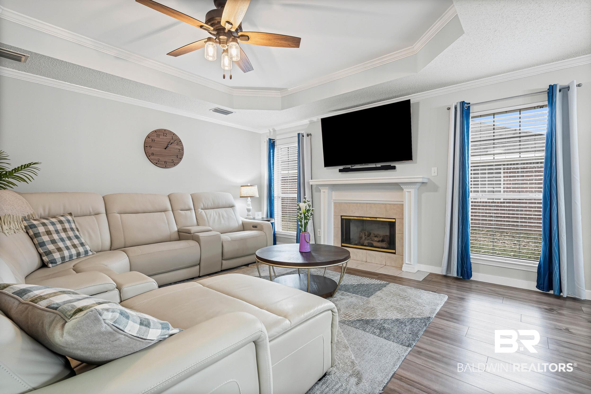 9590 Polo Pl Court Mobile, AL 36695 - Photo 3 of 22 Living area with a tiled fireplace, crown molding, a tray ceiling, plenty of natural light, and wood finished floors