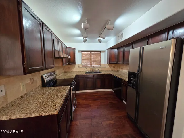 a kitchen with stainless steel appliances granite countertop a refrigerator a sink a stove and a wooden cabinets