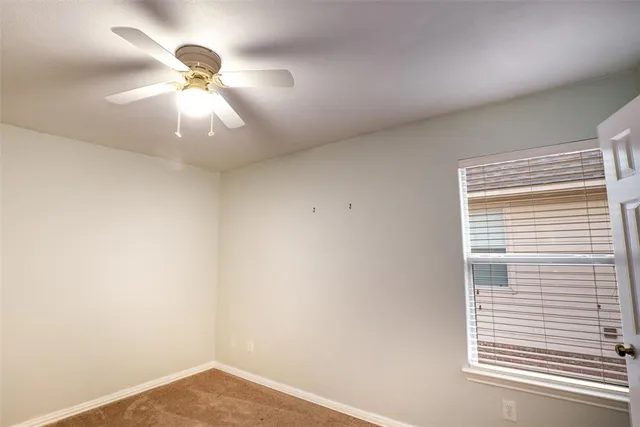 en empty room with a chandelier fan and a window