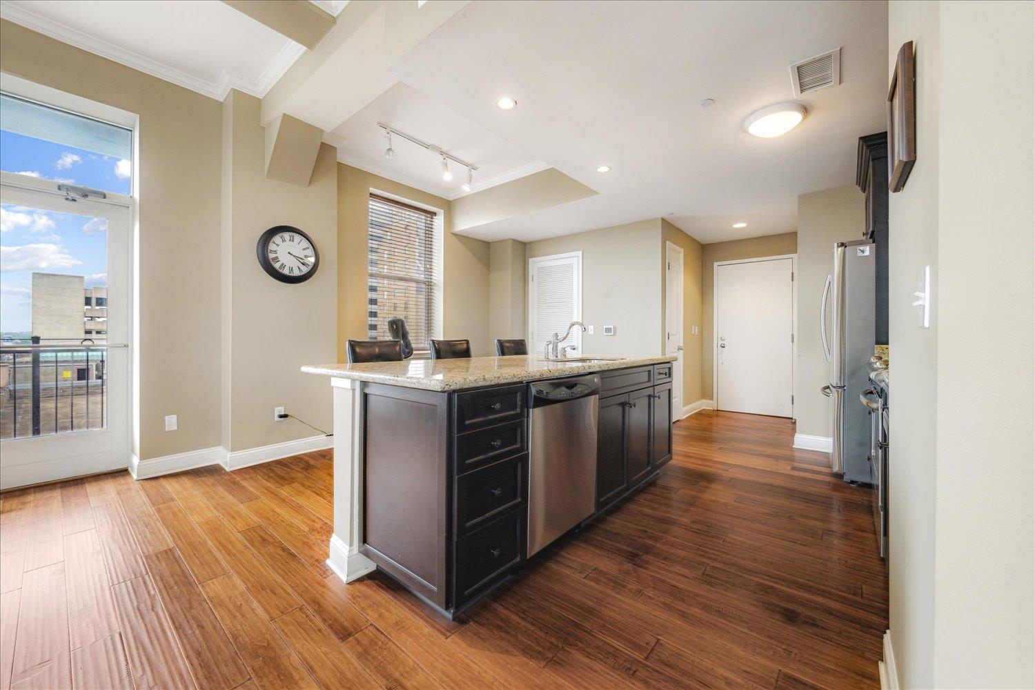 127 Madison Avenue, Unit 602 Memphis, TN 38103 - Photo 15 of 25 Kitchen with stainless steel appliances, an island with sink, dark wood-type flooring, crown molding, and light stone countertops