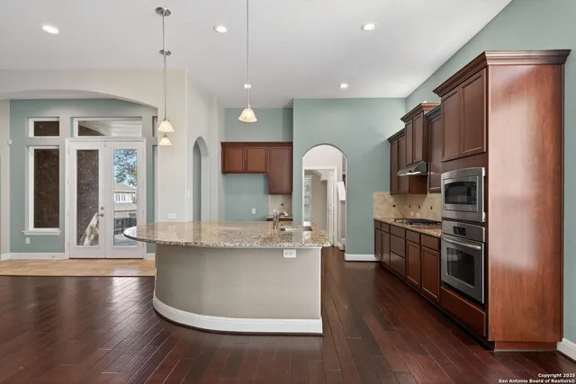 a kitchen with stainless steel appliances granite countertop a refrigerator a stove top oven a sink dishwasher and wooden floor