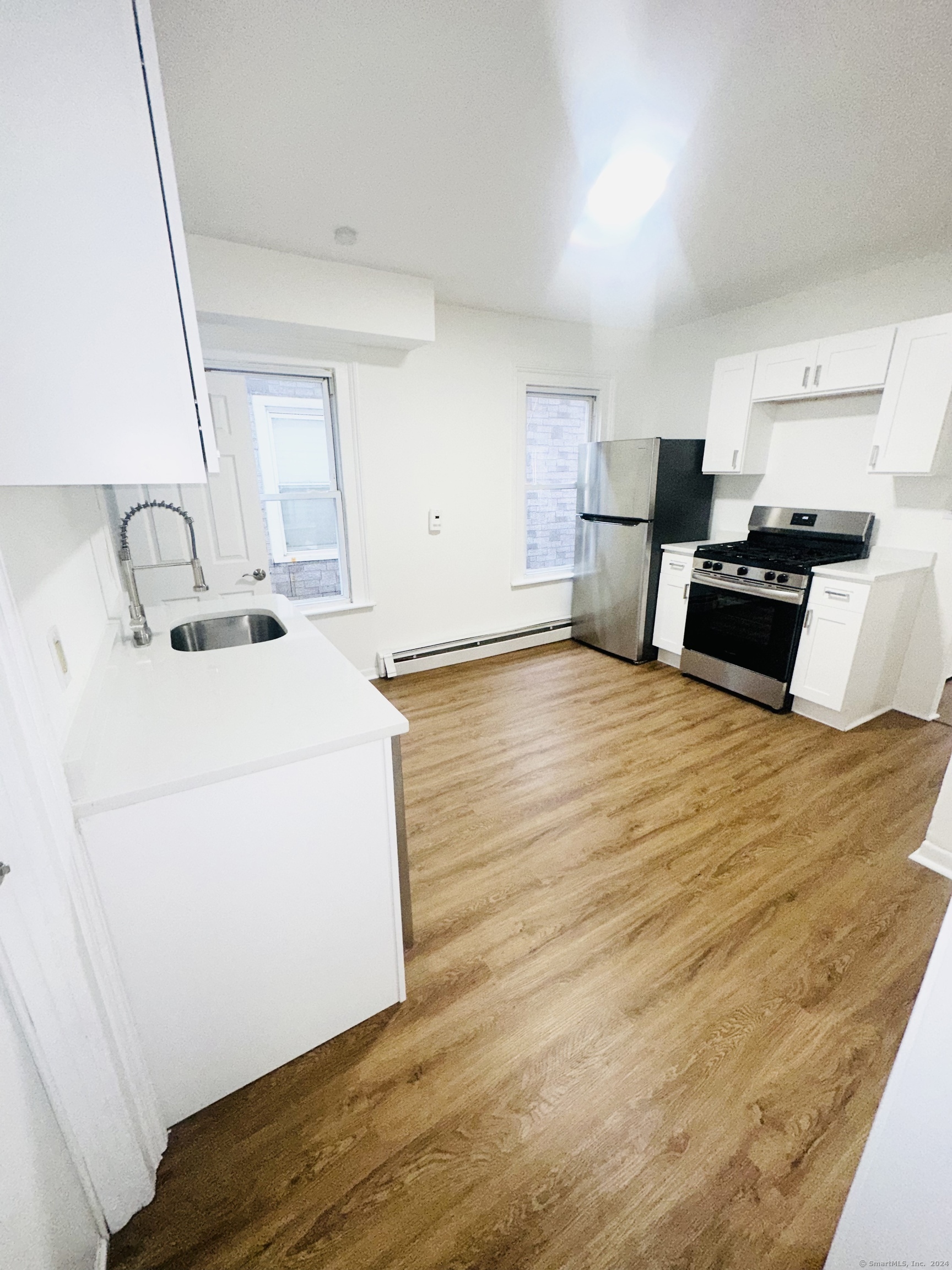 a kitchen with stainless steel appliances kitchen island a stove a refrigerator a sink and white cabinets with wooden floor