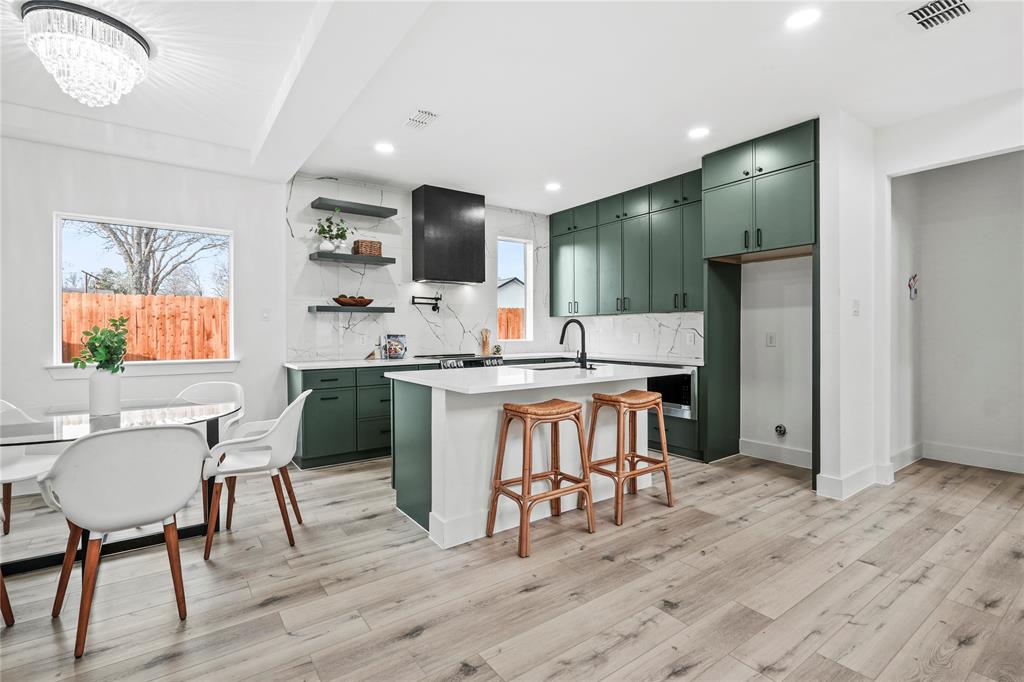 4712 Garrison Street Dallas, TX 75216 - Photo 12 of 30 Kitchen featuring green cabinetry, a breakfast bar area, open shelves, a kitchen island with sink, and decorative backsplash