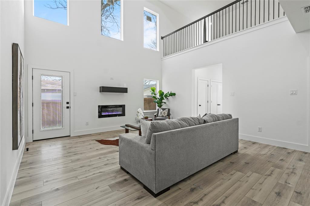 4712 Garrison Street Dallas, TX 75216 - Photo 9 of 30 Living room featuring a glass covered fireplace, healthy amount of natural light, light wood finished floors, and a towering ceiling