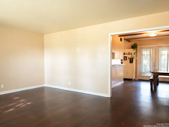 an empty room with wooden floor and windows with curtains