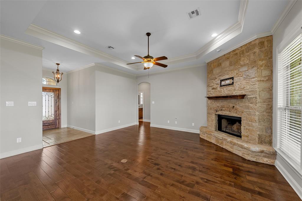 144 Ellis Farm Road Hewitt, TX 76643 - Photo 7 of 36 Spacious living area featuring wood-finish flooring, a stone-faced fireplace with a wood mantel, and a tray ceiling with a ceiling fan