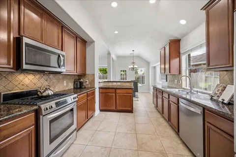 a kitchen with stainless steel appliances granite countertop a stove top oven a sink dishwasher and a microwave oven with large cabinets
