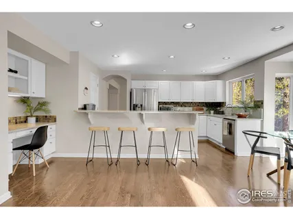 a kitchen with stainless steel appliances kitchen island granite countertop a refrigerator a stove a sink and white cabinets with wooden floor