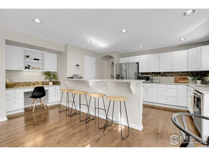 a kitchen with stainless steel appliances granite countertop a refrigerator a stove a sink dishwasher and white cabinets with wooden floor