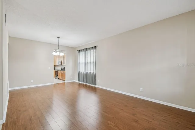 a view of an empty room with wooden floor kitchen view and a window
