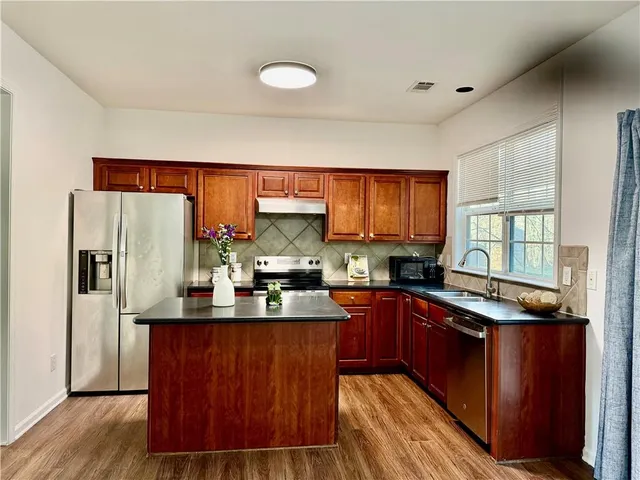 a kitchen with stainless steel appliances granite countertop a refrigerator a sink dishwasher a stove with wooden cabinets and floor