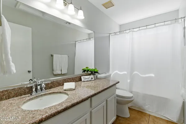 a bathroom with a granite countertop sink a toilet a mirror a shower and vanity