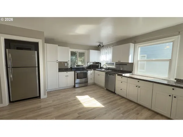 a kitchen with stainless steel appliances granite countertop a refrigerator a stove and a sink with wooden floors