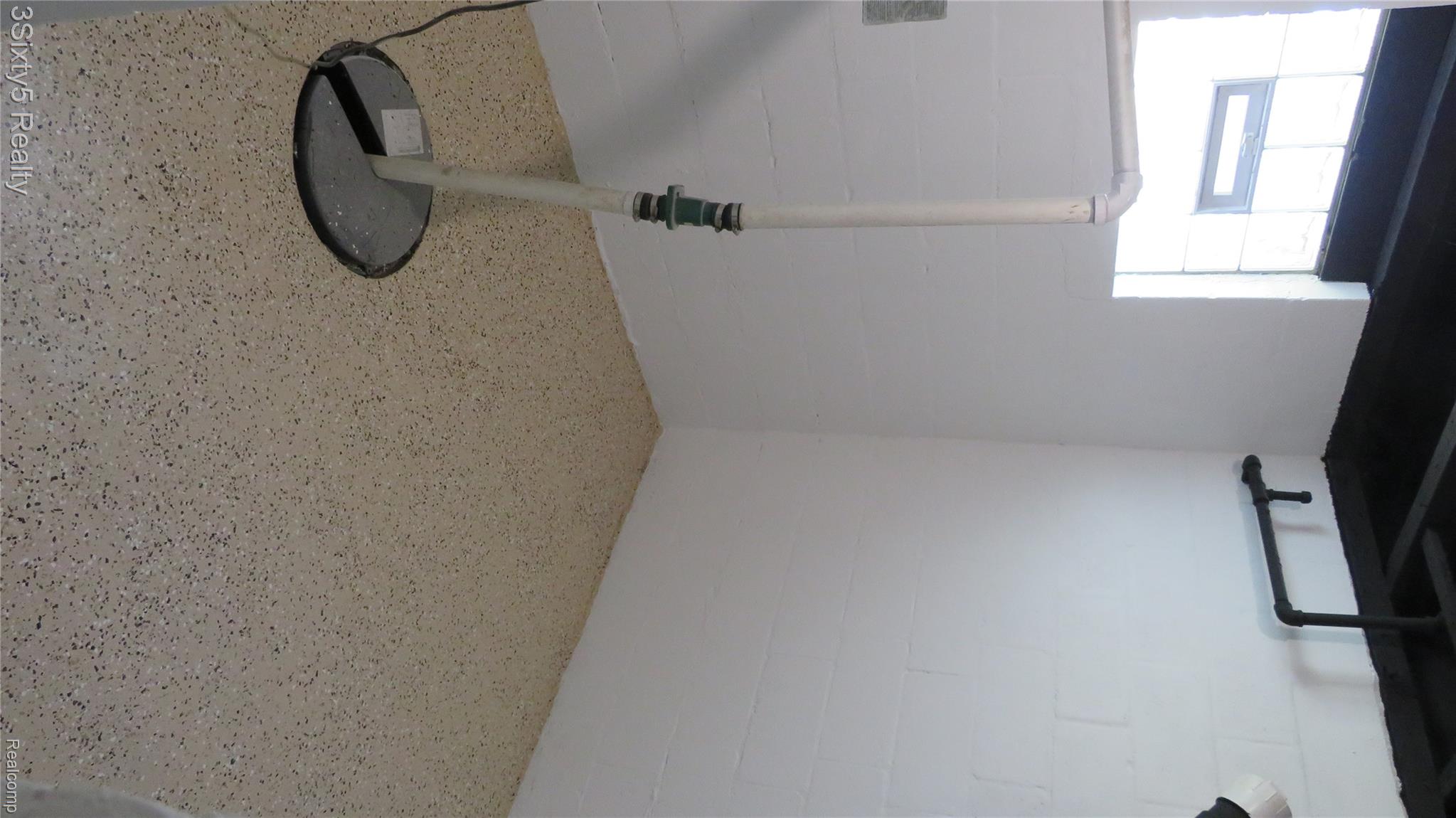 16558 Haggerty Road Belleville, MI 48111 - Photo 31 of 40 Finished basement area featuring white-painted block walls, exposed black-painted ceiling joists, a glass block window, and speckled epoxy flooring