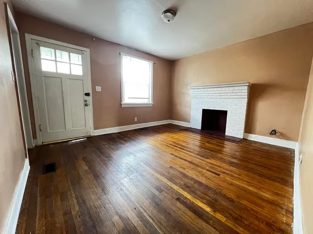 an empty room with wooden floor fireplace and windows