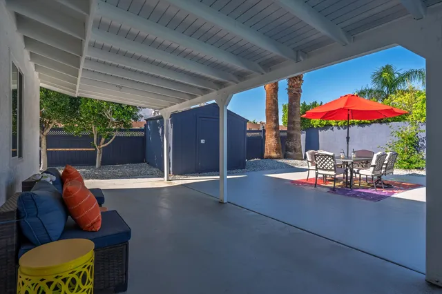 a view of a patio with table and chairs under an umbrella with a barbeque