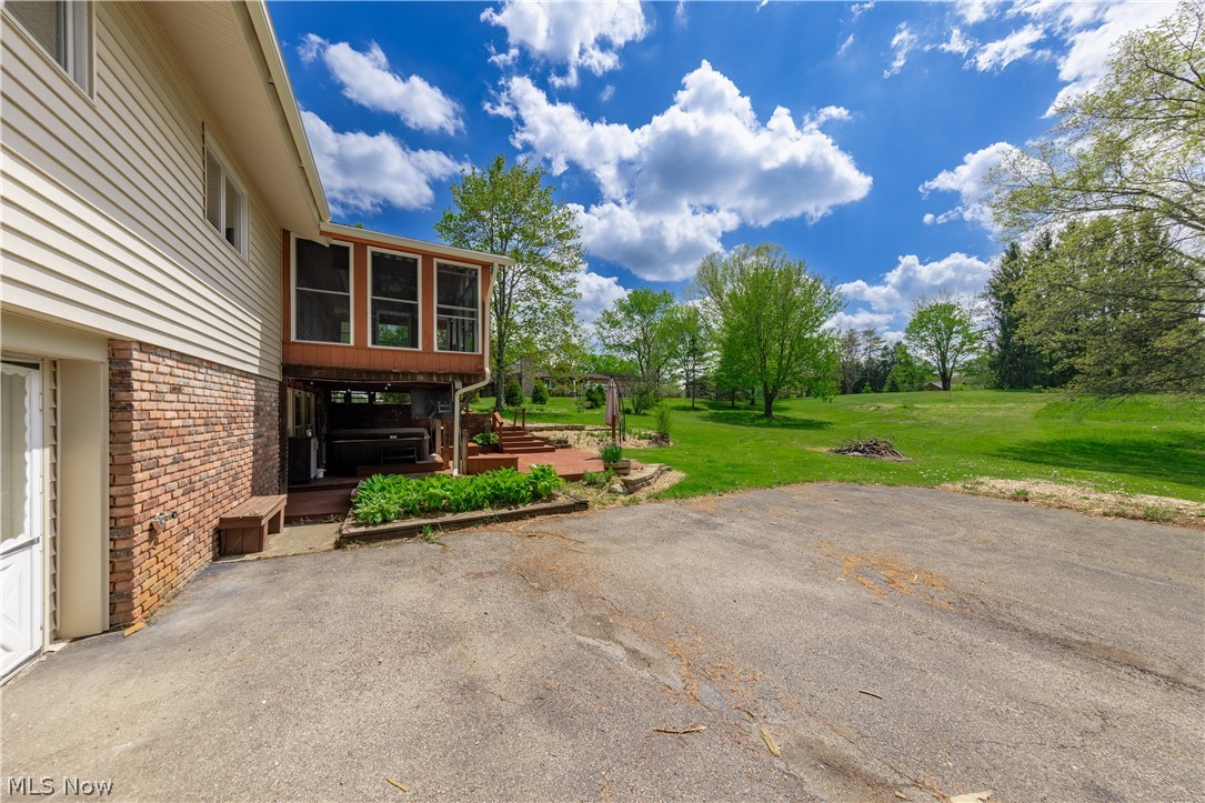 7969 Dines Road Novelty, OH 44072 - Photo 44 of 48 Back of the home with large paved area leading to the partially covered deck with a hot tub, wooden deck, and expansive backyard