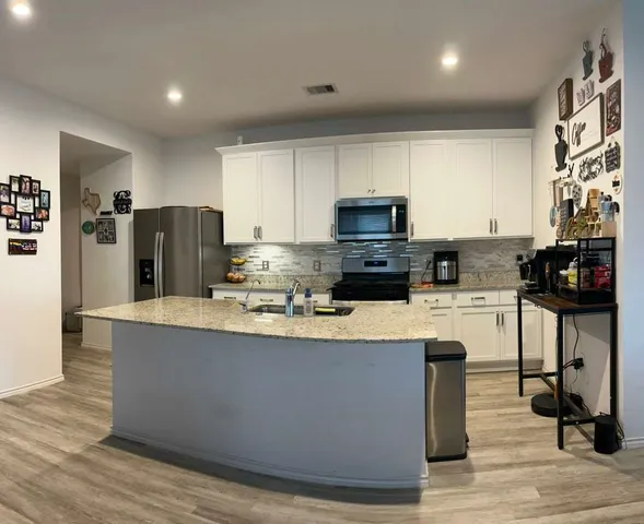 a kitchen with stainless steel appliances granite countertop a stove a sink a refrigerator and white cabinets with wooden floor