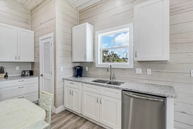 a kitchen with a sink dishwasher and white cabinets with wooden floor
