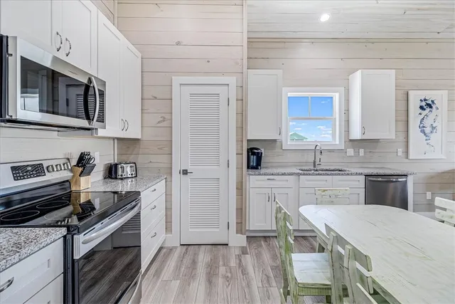 a kitchen with stainless steel appliances granite countertop a stove top oven a sink dishwasher a refrigerator and white cabinets with wooden floor