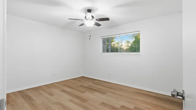 an empty room with wooden floor chandelier fan and windows
