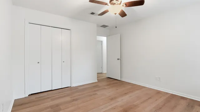 an empty room with wooden floor fan and windows