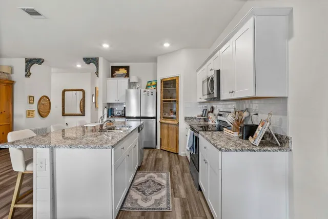 a kitchen with stainless steel appliances granite countertop a stove top oven a sink a refrigerator white cabinets and wooden floor