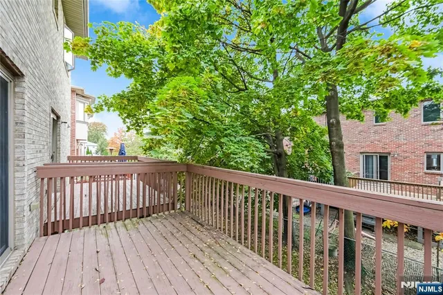 a view of a white house with a small deck and a large tree