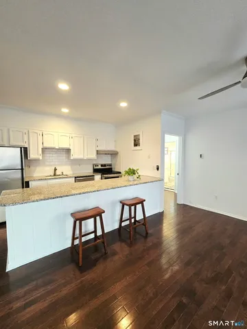 a open kitchen with stainless steel appliances granite countertop a stove top oven a sink dishwasher and white cabinets with wooden floor