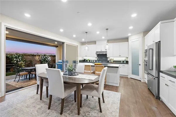 a kitchen with stainless steel appliances a refrigerator a stove a center island a wooden floor and white cabinets