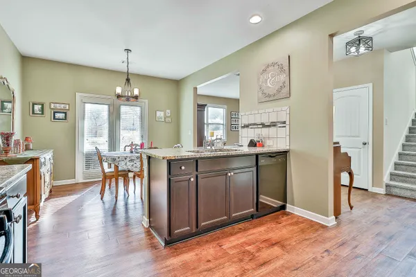 a kitchen with stainless steel appliances granite countertop a refrigerator a sink dishwasher a dining table and chairs with wooden floor