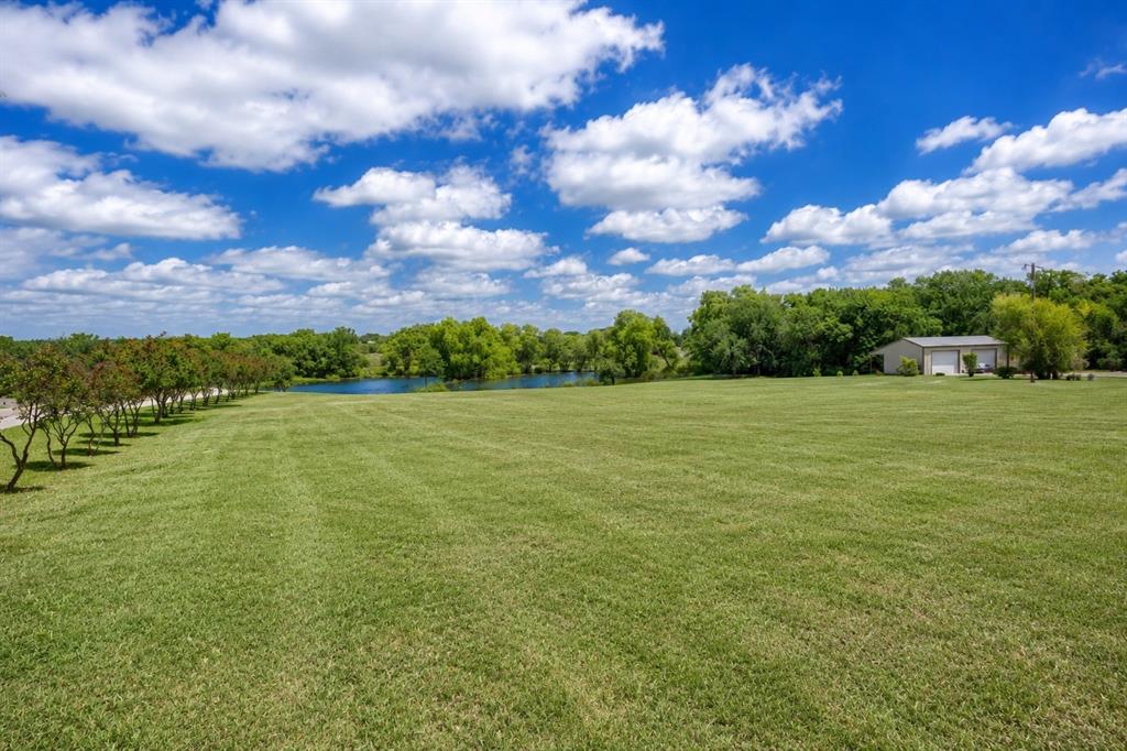 900 Hodgins Road Van Alstyne, TX 75495 - Photo 8 of 10 Expansive green lawn with a tree-lined perimeter, a visible body of water, and a two-door outbuilding