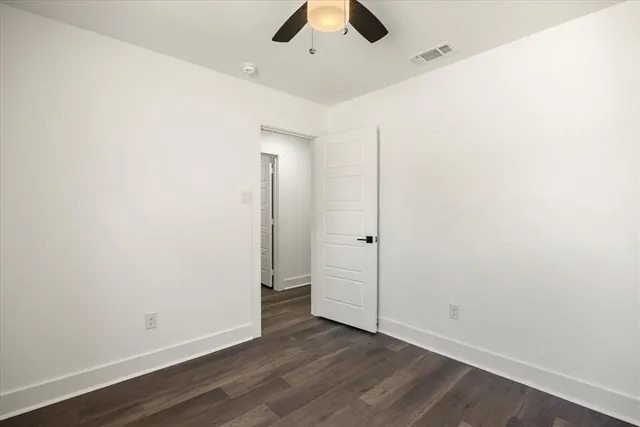 an empty room with wooden floor chandelier fan and windows