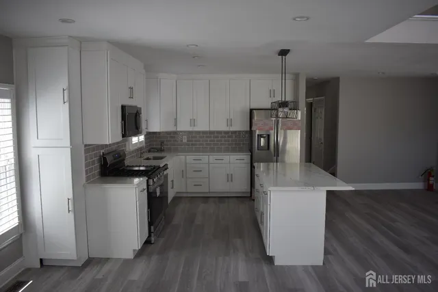 a kitchen with stainless steel appliances a refrigerator a stove a sink and white cabinets with wooden floor