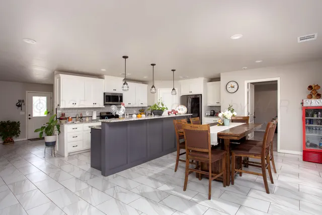 a room with stainless steel appliances kitchen island granite countertop a table chairs and a stove top oven