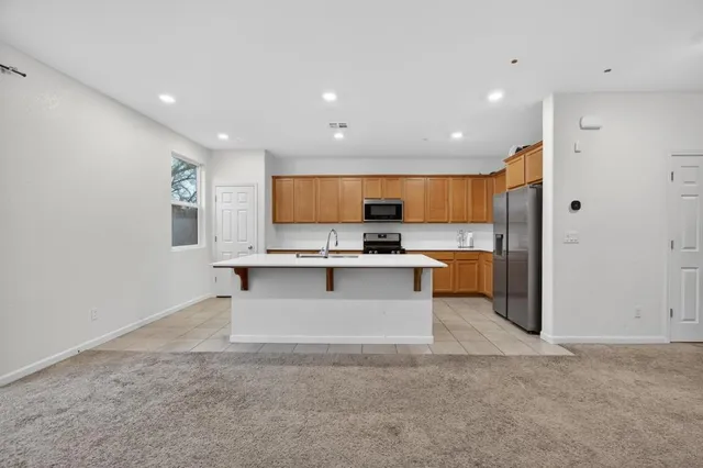 a large white kitchen with kitchen island a sink a center island stainless steel appliances and a refrigerator