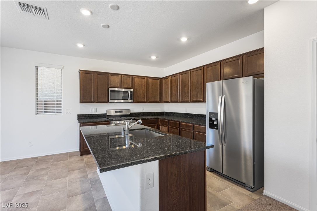 5646 Spring Trellis Street Las Vegas, NV 89113 - Photo 3 of 25 Kitchen featuring dark brown cabinets, appliances with stainless steel finishes, dark stone countertops, an island with sink, and recessed lighting