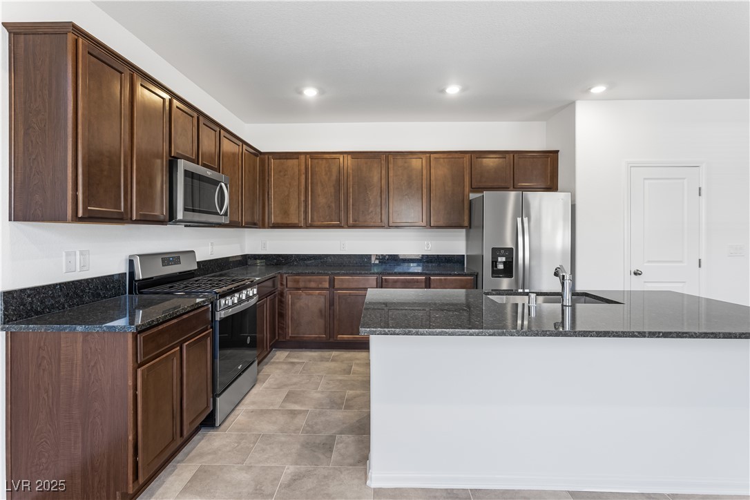 5646 Spring Trellis Street Las Vegas, NV 89113 - Photo 4 of 25 Kitchen with appliances with stainless steel finishes, dark stone counters, dark brown cabinetry, recessed lighting, and a center island with sink