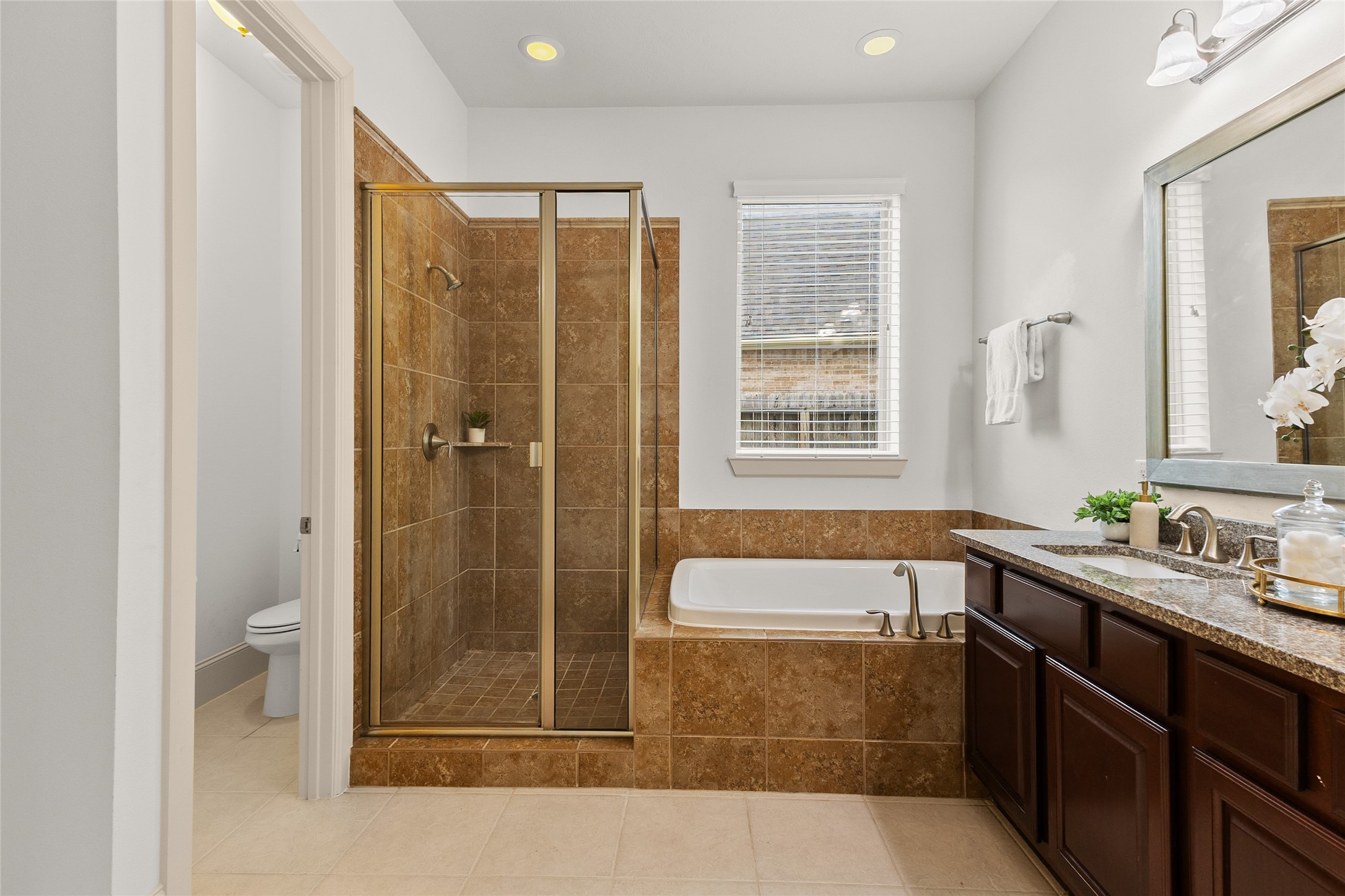 3302 Rochdale Street Houston, TX 77025 - Photo 26 of 50 This primary bathroom offers a functional layout with a separate glass enclosed shower and soaking tub, giving you options for your daily routine. Granite countertops, a dual sink vanity, and a private water closet complete the space, while natural light from the window adds a bright, airy feel. It's a well equipped retreat designed for everyday comfort.