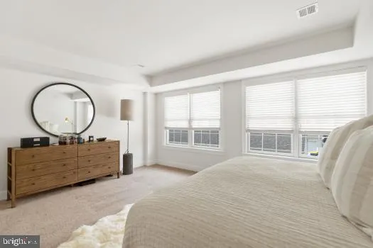 a bedroom with a bed a mirror on dresser and a large window