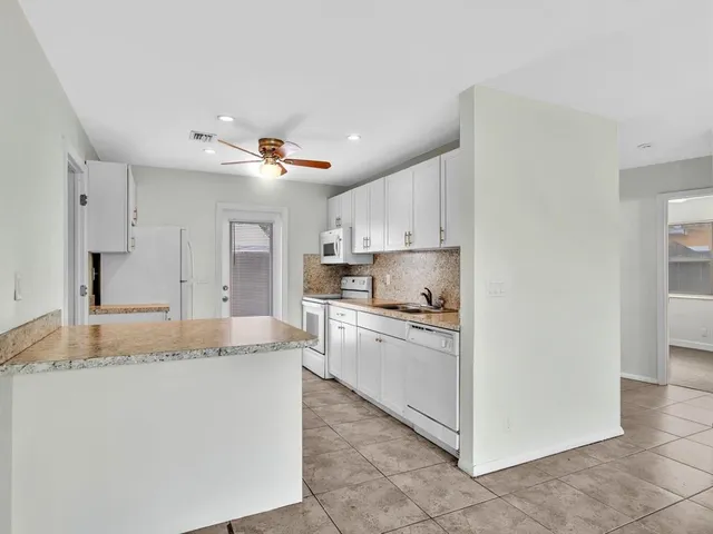 a kitchen with kitchen island granite countertop a sink a stove a refrigerator and white cabinets