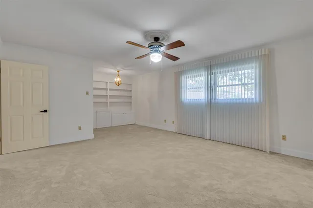 an empty room with chandelier fan and windows