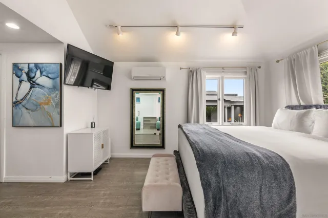 a spacious bedroom with a bed and a flat tv screen on the dresser