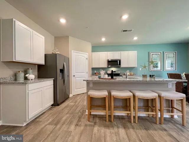 a kitchen with stainless steel appliances granite countertop a refrigerator a sink dishwasher a stove and white cabinets with wooden floor