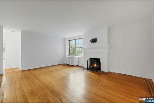 a view of an empty room with wooden floor fireplace and a window