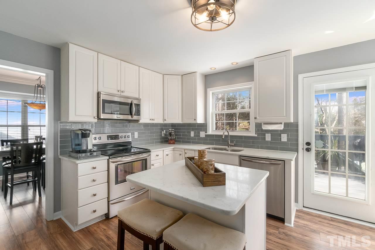 8727 Harps Mill Road Raleigh, NC 27615 - Photo 7 of 25 a kitchen with a stove a sink dishwasher a microwave oven and a dining table with wooden floor
